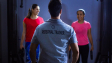 Back view of a personal trainer guiding two women during a gym session indoors.